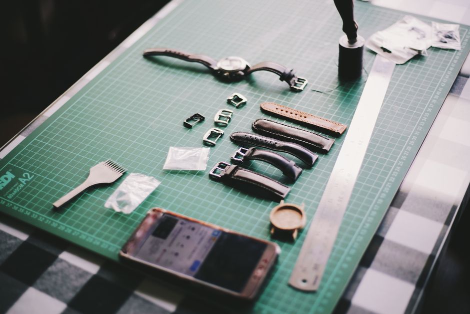 Close-up of watchmaking tools and leather straps on a crafting table.