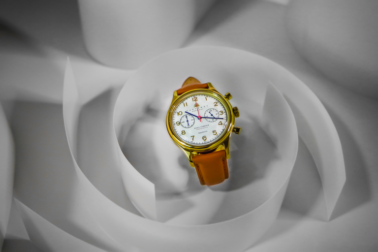 Close-up view of a luxury wristwatch with a gold case and leather strap, set against a white background.